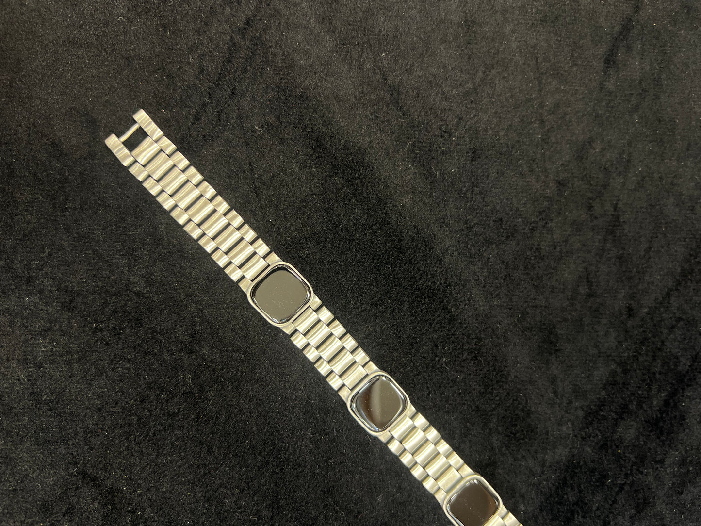 Metallic bracelet with a black square charm on a dark textured background