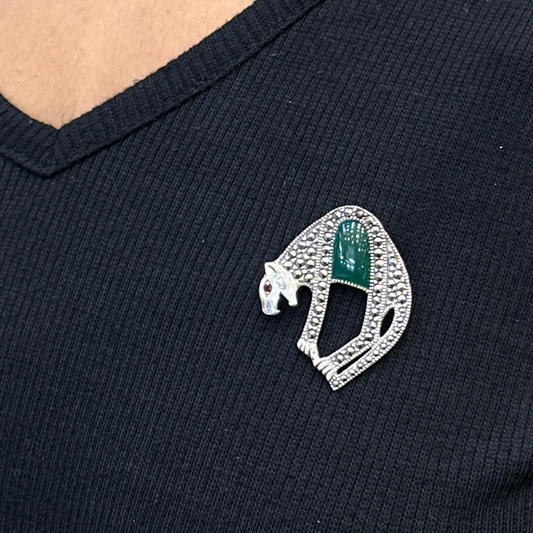 Close-up of a black shirt with a decorative brooch featuring a green gemstone and silver detailing.