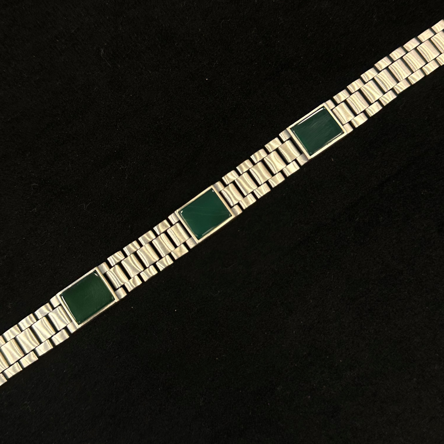 Silver bracelet with green square stones on a black background