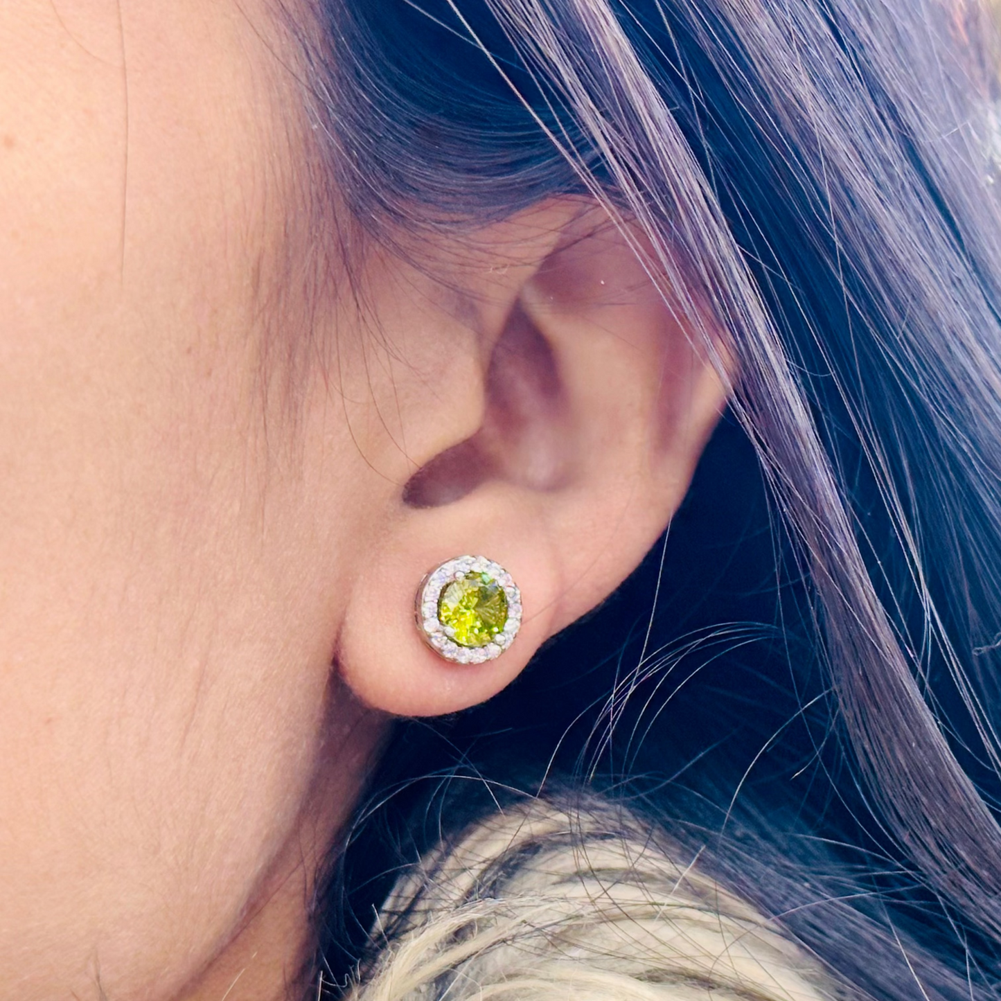 Close-up of an ear wearing a yellow gemstone stud earring with blurred background