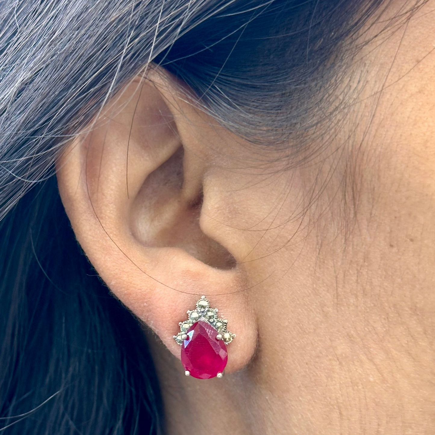 Close-up of an ear wearing a red teardrop earring with a silver setting.