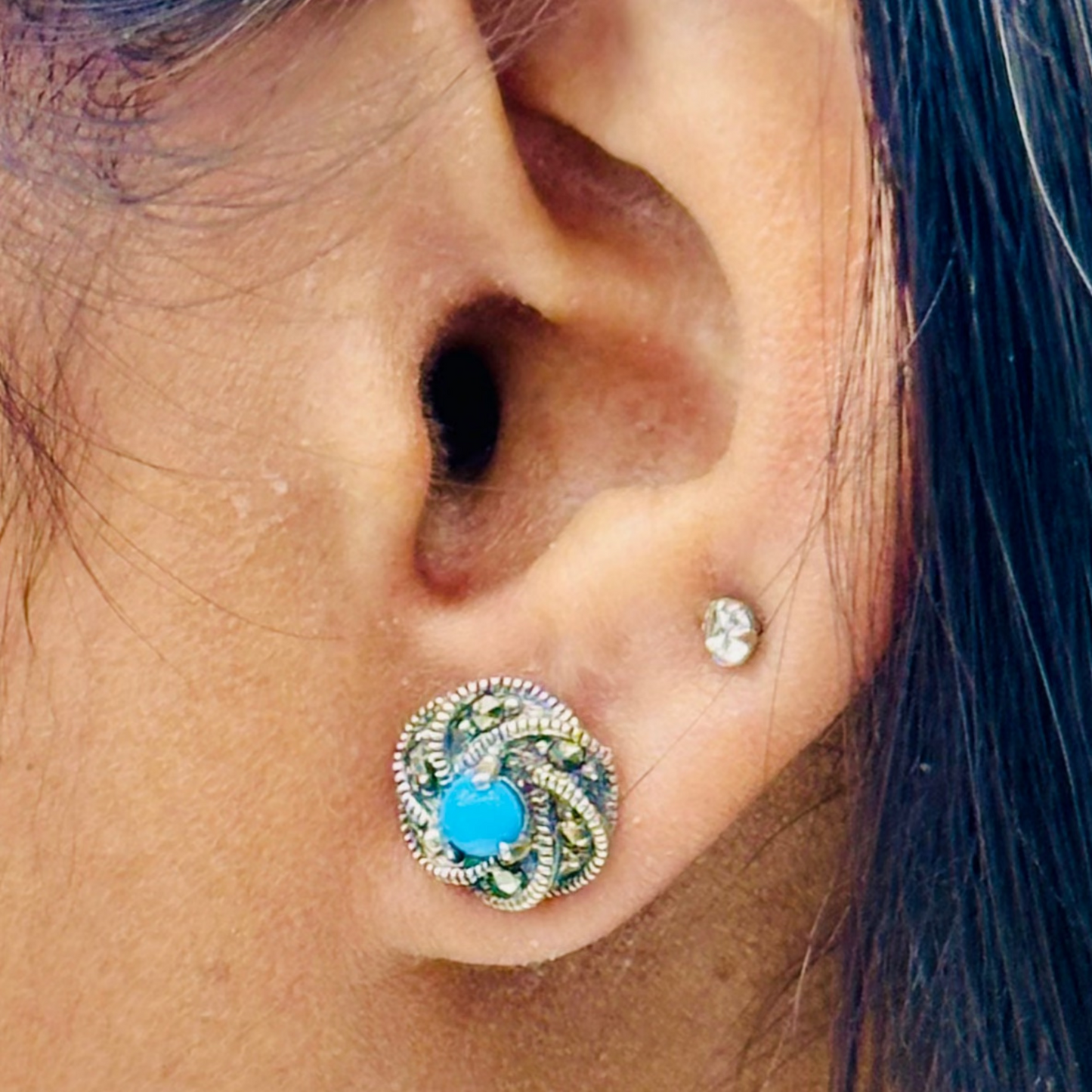 Close-up of an ear wearing a decorative earring with a blue gemstone.