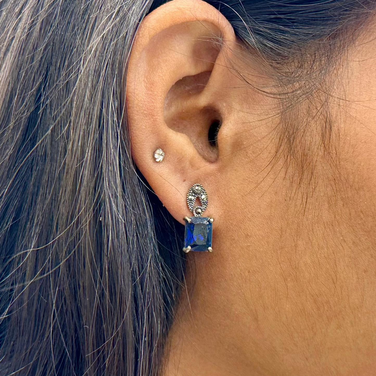 Close-up of an ear wearing a blue gemstone earring with a blurred background