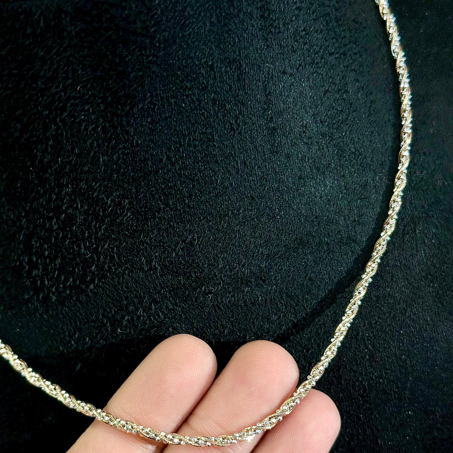 Silver rope chain held by a hand against a black background