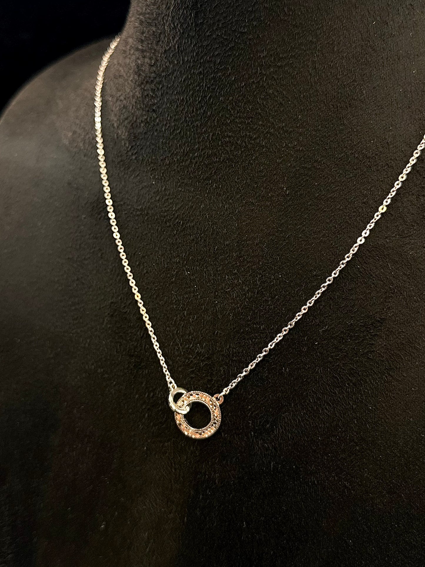 Silver necklace with a circular pendant on a black mannequin.