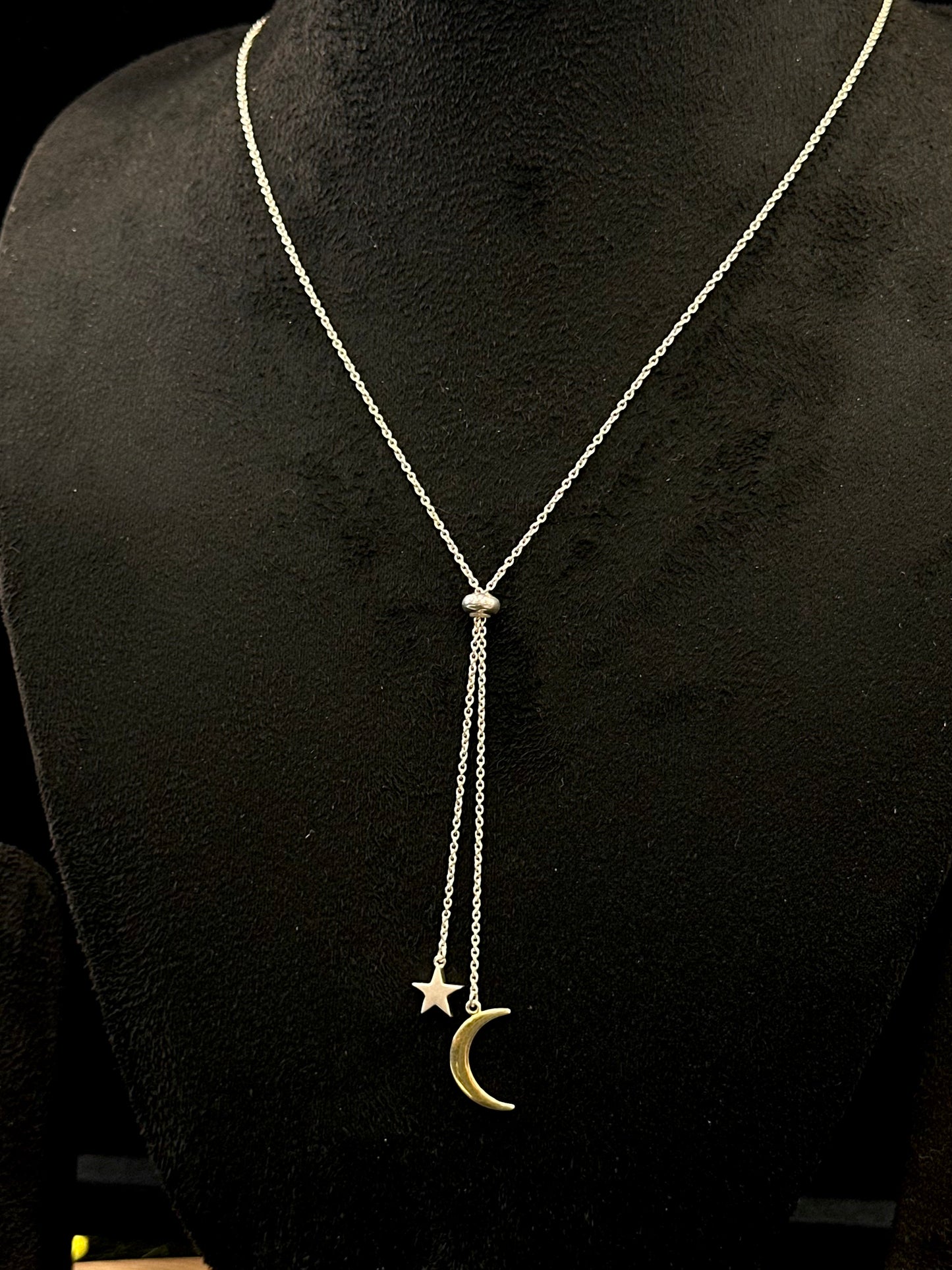 Silver necklace with star and moon pendant on a black background