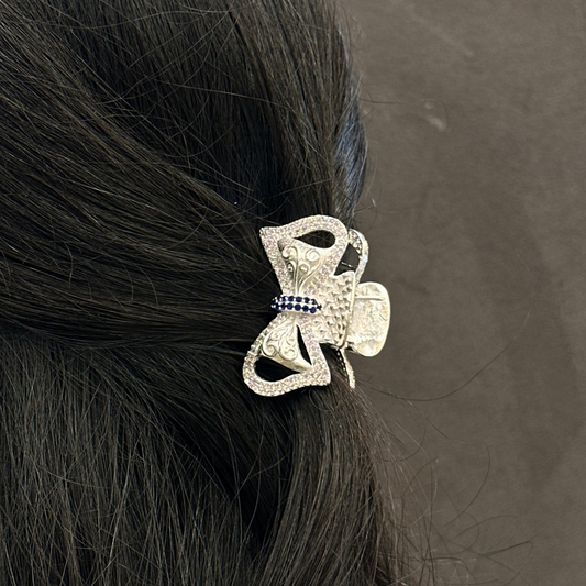 Silver hair clip with decorative elements on black hair against a gray background