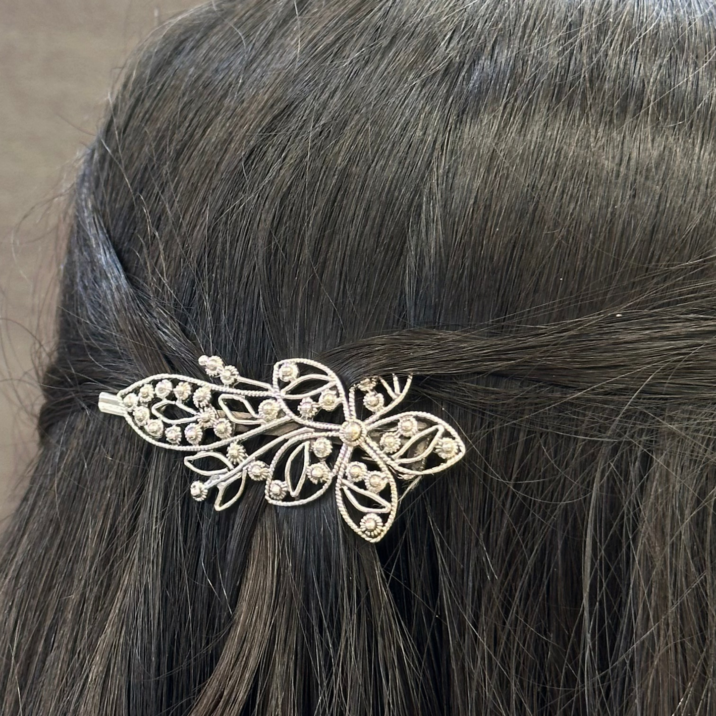 Silver hair clip on a person's hair against a neutral background