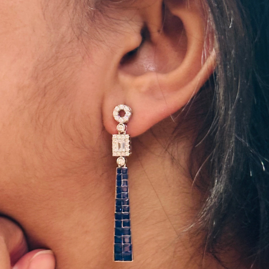 a pair of emerald blue tassel earrings. They feature a silver base, sparkling cubic zirconia, and deep blue gemstone tassels.