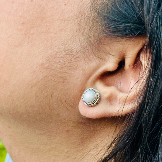 Elegant silver stud earrings featuring a luminous pearl in an intricate frame.