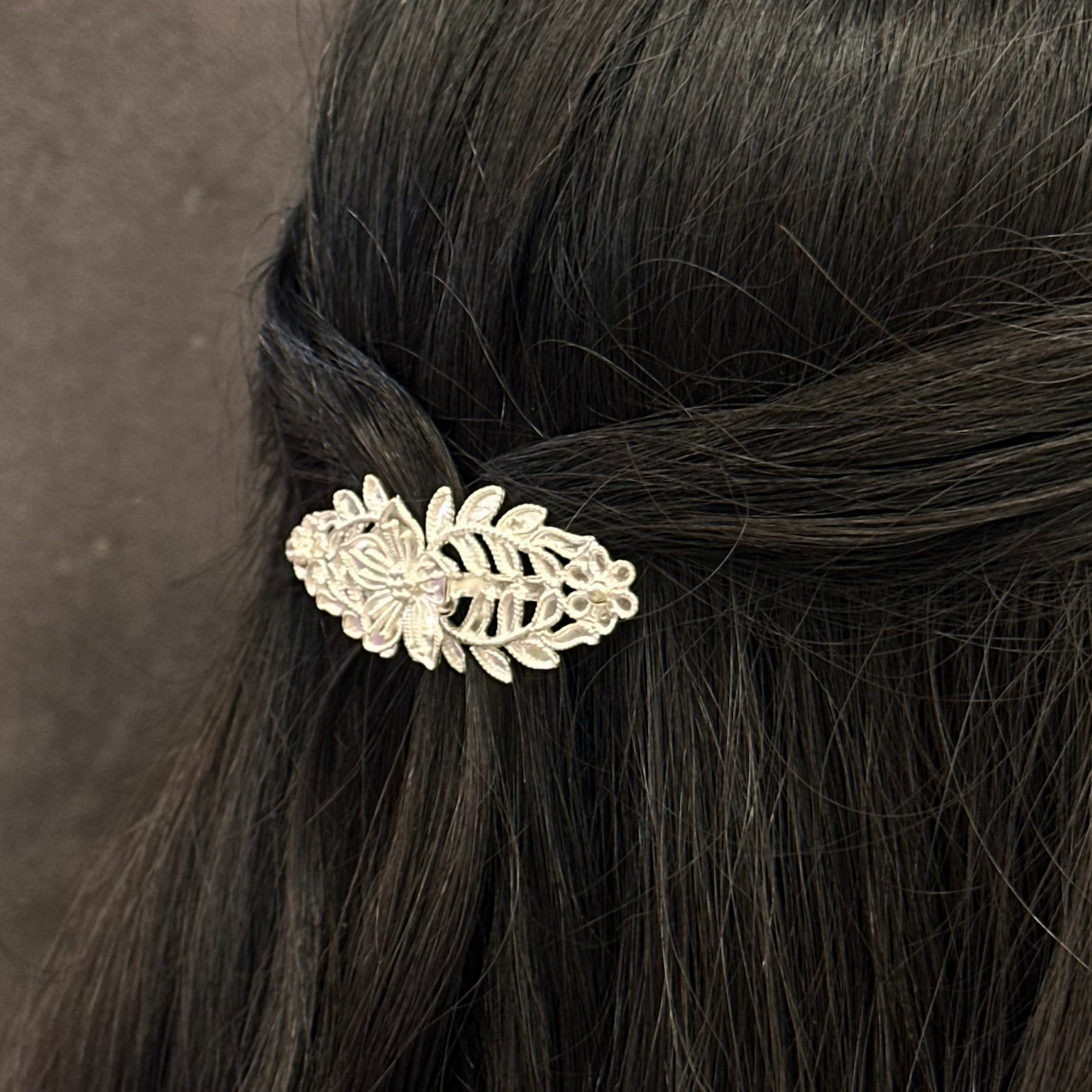 Hair accessory with leaf design in a person's hair against a gray background