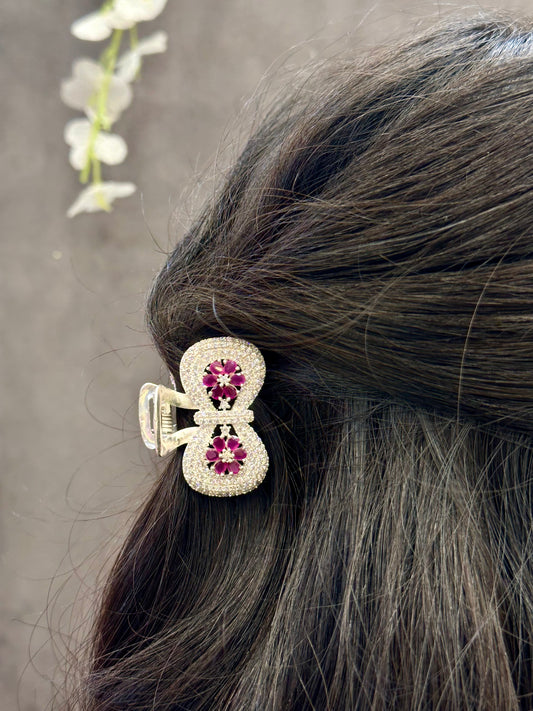 Close-up of a hair clip with gemstones in a bow shape on dark hair against a neutral background.
