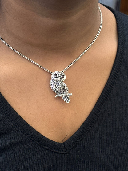 Silver owl pendant necklace on a person wearing a black top.