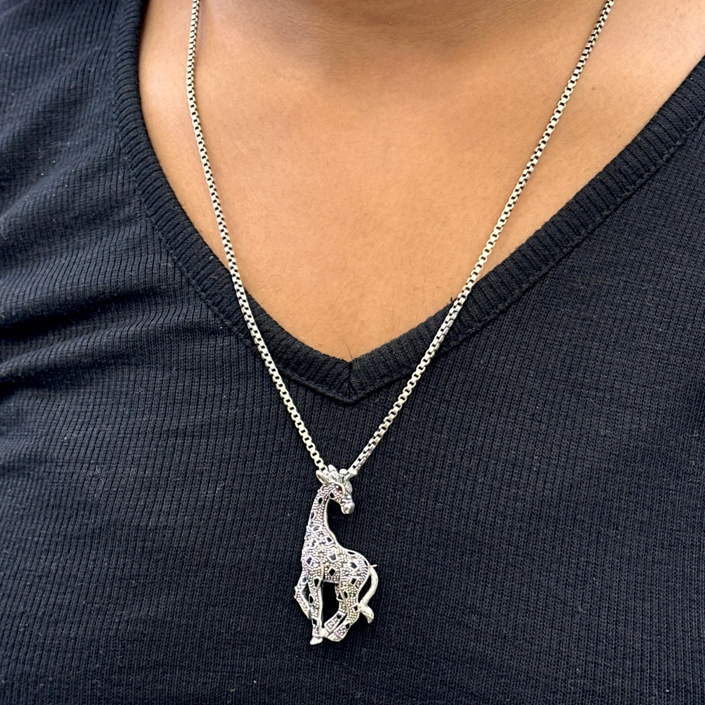 Silver giraffe pendant necklace on a person wearing a black top.