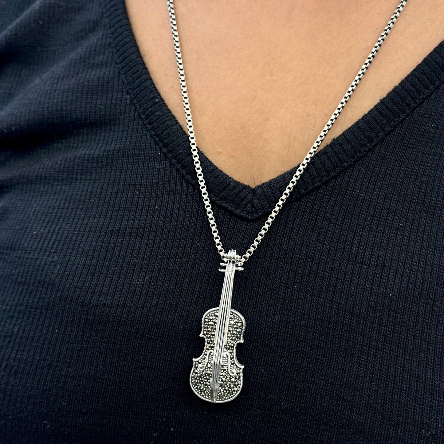 Silver violin pendant necklace on a person wearing a black top