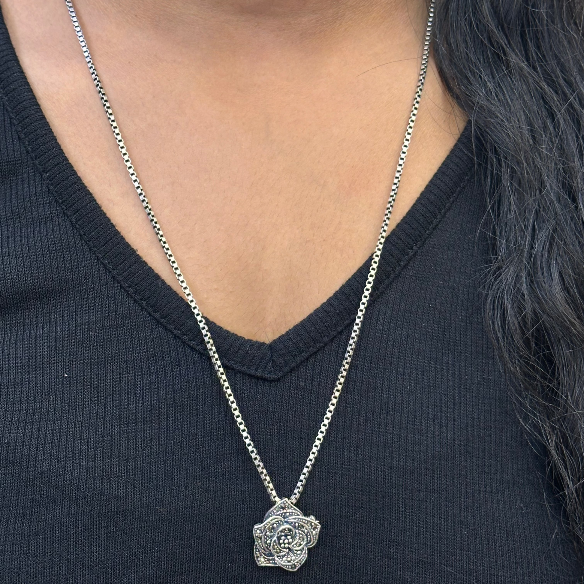 Person wearing a silver necklace with a pendant on a black shirt