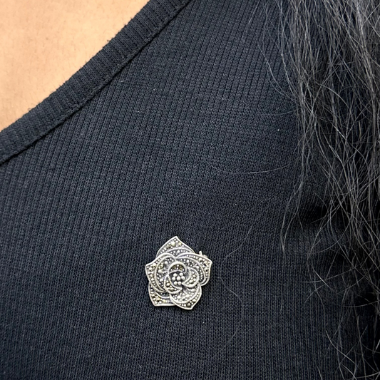 Person wearing a black top with a silver brooch on a neutral background