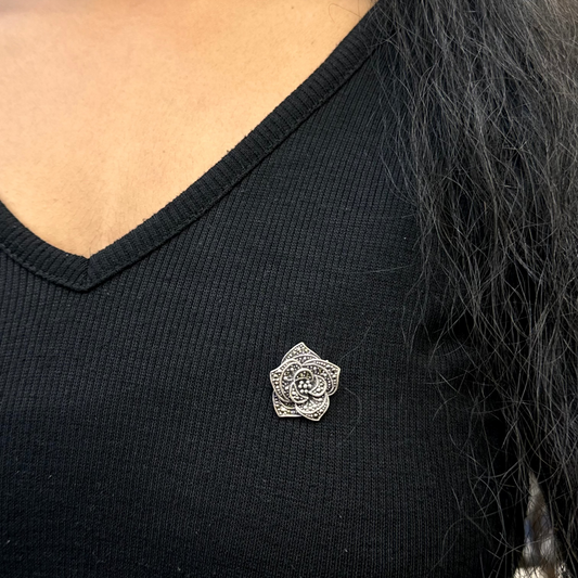Person wearing a black V-neck shirt with a silver brooch on the chest.