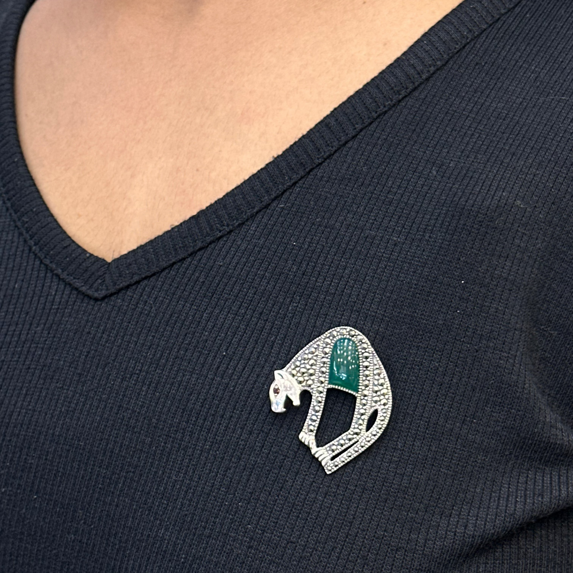 Person wearing a black shirt with a decorative brooch featuring a green gemstone and silver detailing.
