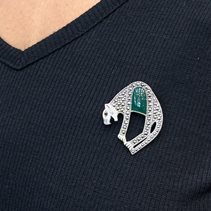 Close-up of a black shirt with a decorative brooch featuring a green gemstone and silver detailing.