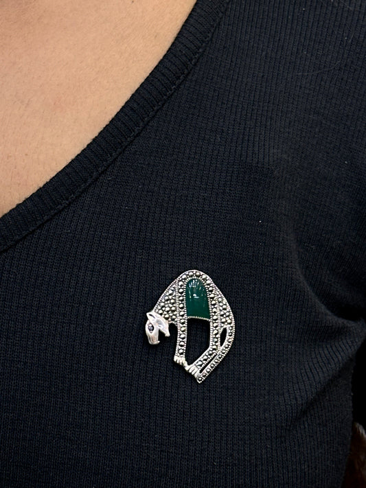 Close-up of a black garment with a decorative brooch featuring green and silver elements.