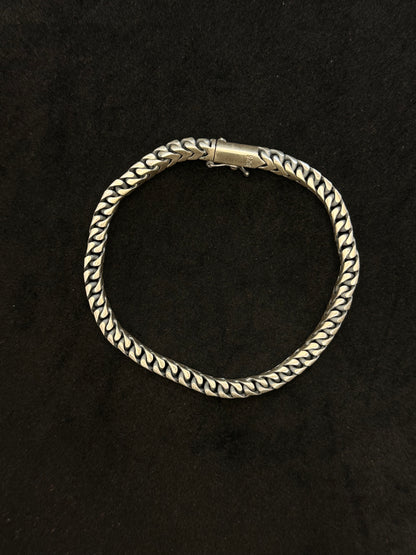 Silver bracelet with braided design on a black background