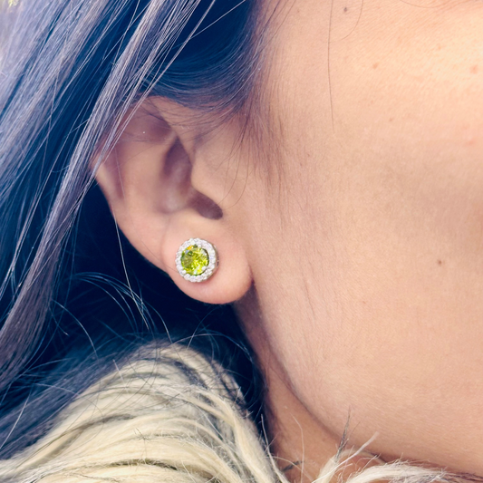 Close-up of an ear wearing a green gemstone stud earring with blurred background
