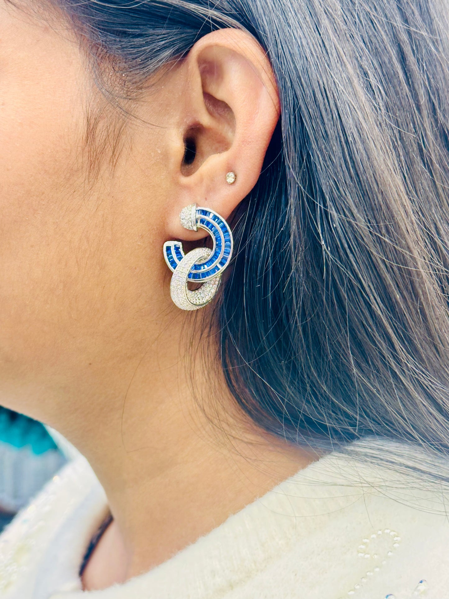 Close-up of a person wearing a blue and silver earring with blurred background