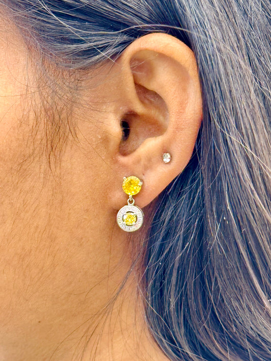 Close-up of an ear wearing a yellow earring with a blue hair background