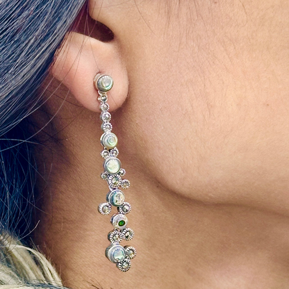 Close-up of an ear wearing a dangling earring with pearls and gemstones.
