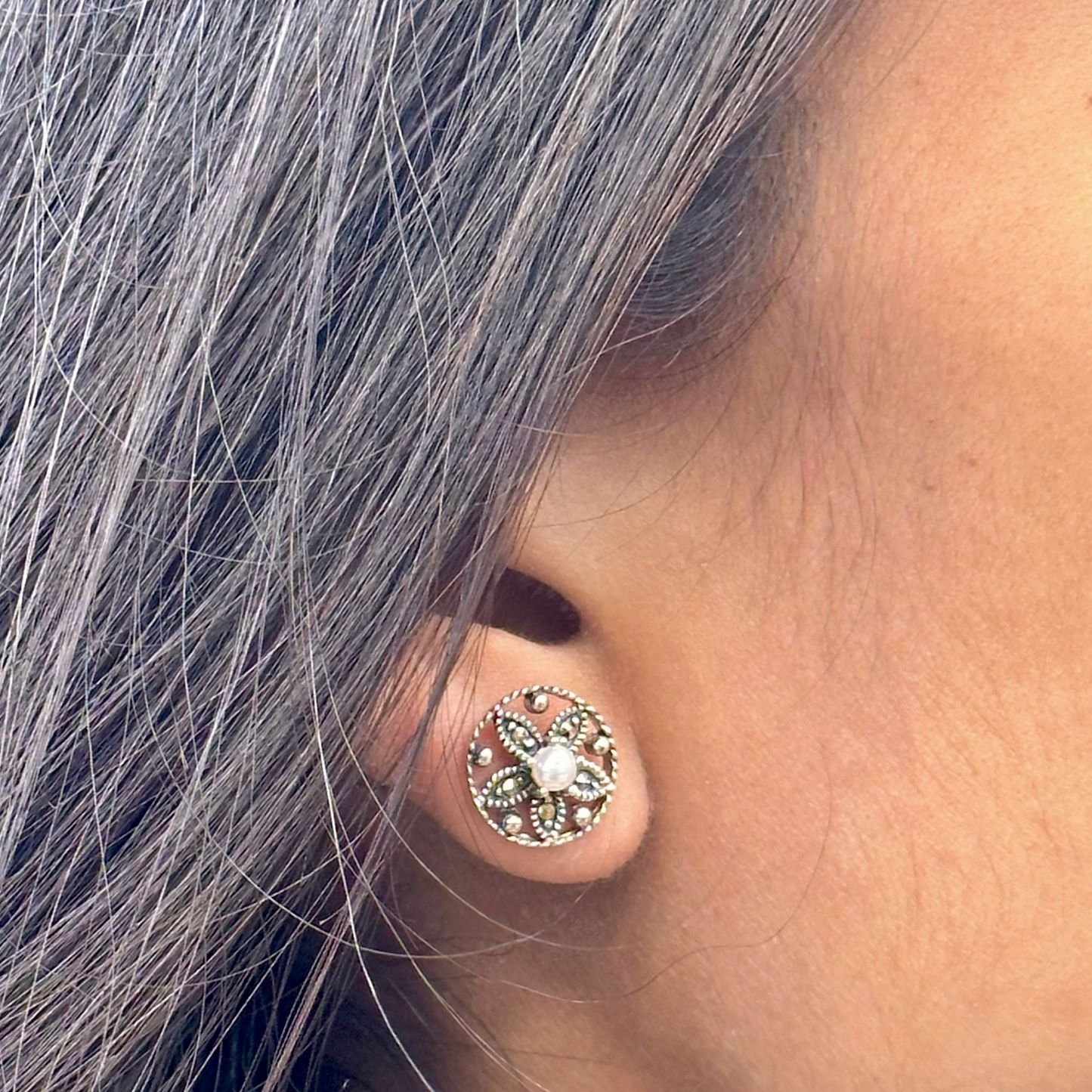 Close-up of an ear wearing a decorative stud earring with gray hair.