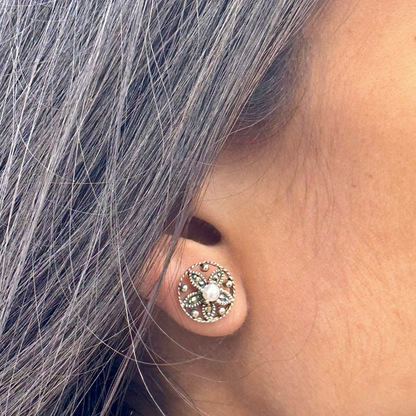 Close-up of an ear wearing a decorative stud earring with gray hair.