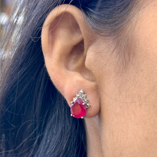 Close-up of an ear wearing a red gemstone earring with a diamond setting.