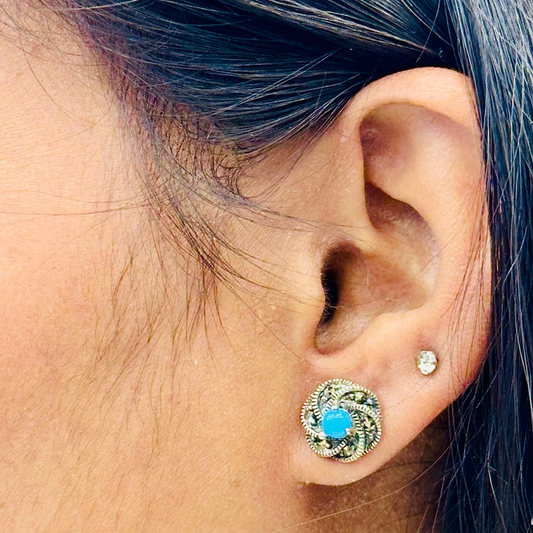 Close-up of an ear wearing a decorative earring with a blue gemstone.