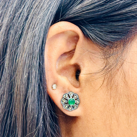 Close-up of an ear wearing a silver earring with a green gemstone, hair partially covering the face.