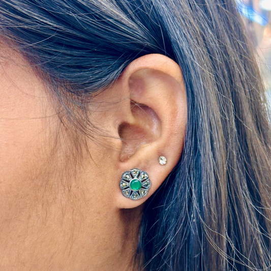 Close-up of an ear wearing a silver earring with green gemstone, hair color is blue.