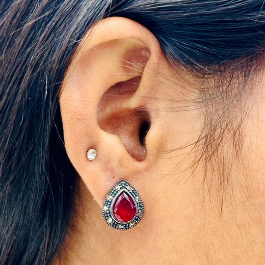 Close-up of an ear wearing a red teardrop earring with a blurred background