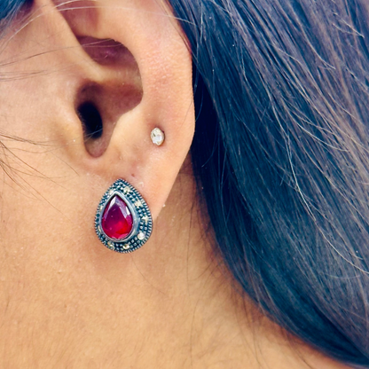 Close-up of an ear wearing a red gemstone earring with a silver setting.