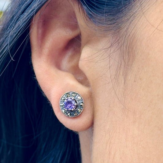 Close-up of an ear wearing a stud earring with a purple gemstone, blurred background