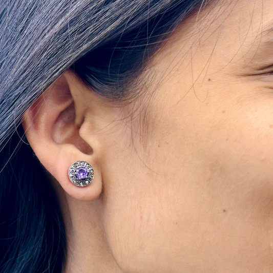 Close-up of an ear wearing a purple gemstone earring with a blurred background