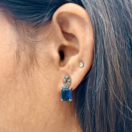 Close-up of an ear wearing a blue gemstone earring with a blurred background