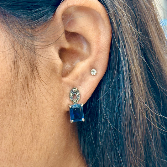 Close-up of an ear wearing a blue gemstone earring with a blurred background