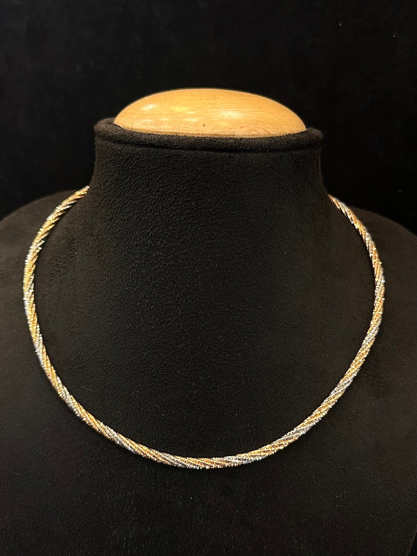 Gold necklace on a black mannequin bust with a wooden top against a dark background