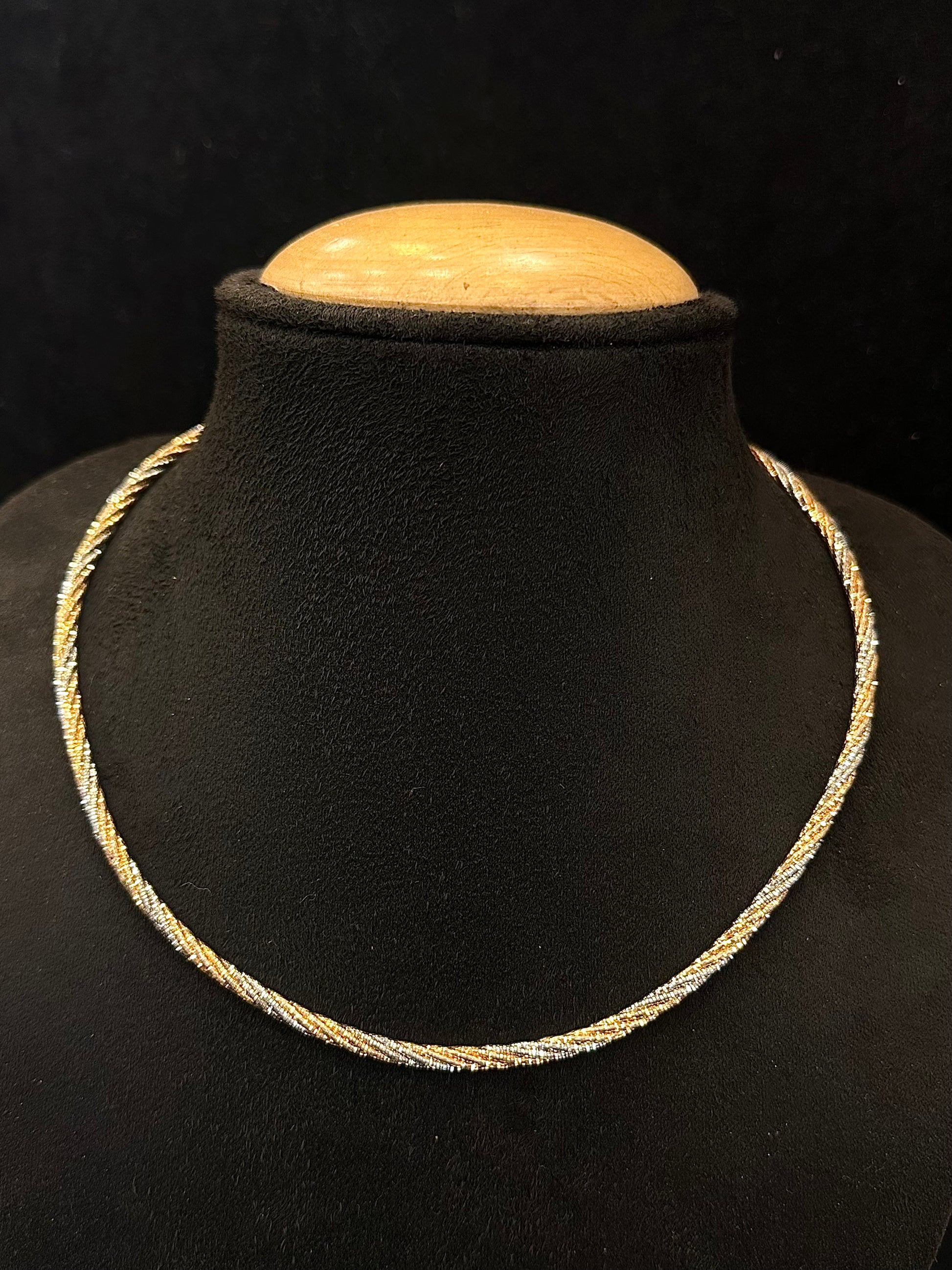 Gold necklace on a black mannequin bust with a wooden top against a dark background