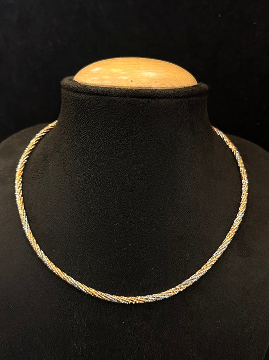 Gold necklace on a black mannequin bust with a wooden top against a dark background