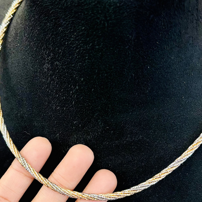 Gold necklace on a black velvet stand with a hand holding it for scale.