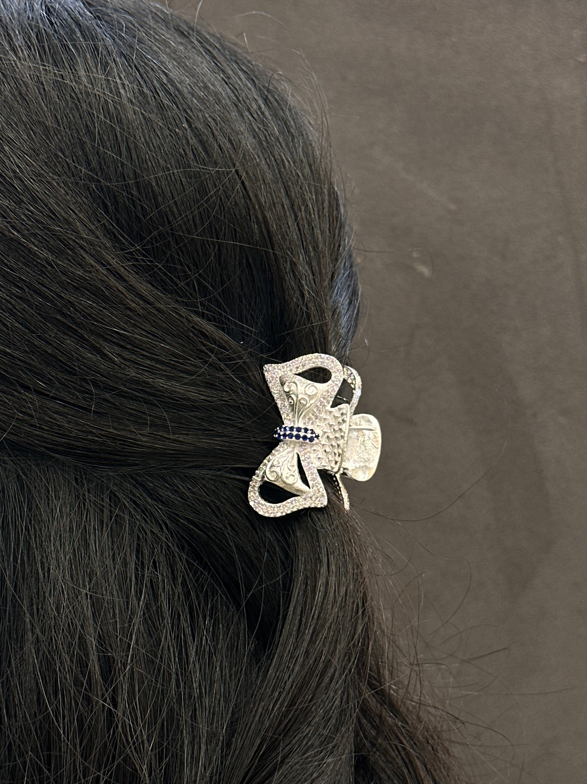 Silver hair clip with decorative elements on black hair against a gray background