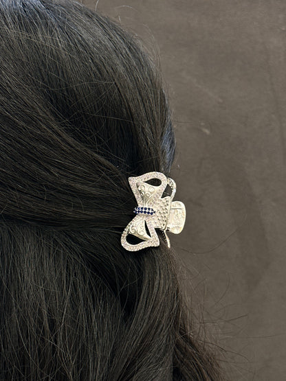 Silver hair clip with decorative elements on black hair against a gray background