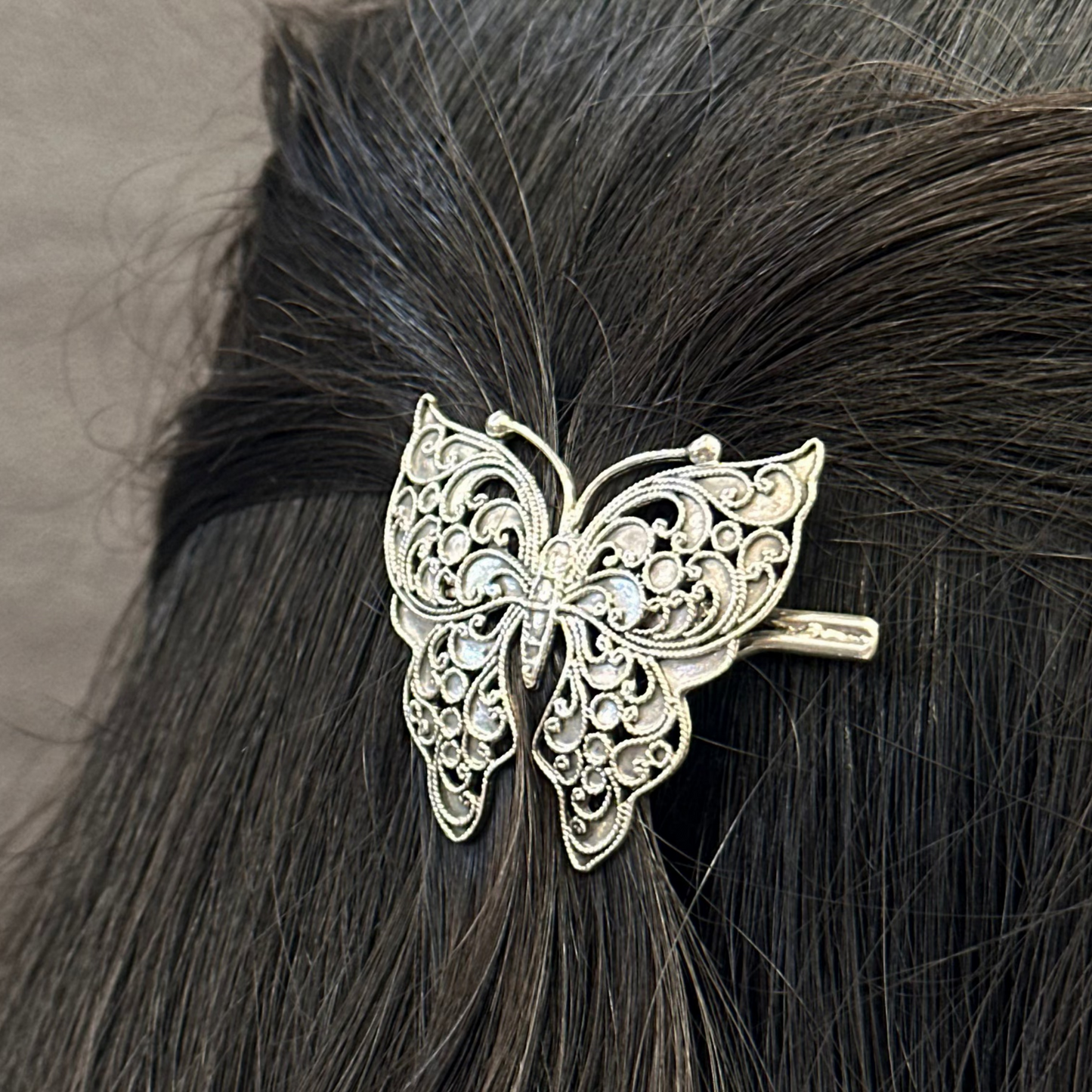 Silver butterfly hair clip on black hair against a neutral background