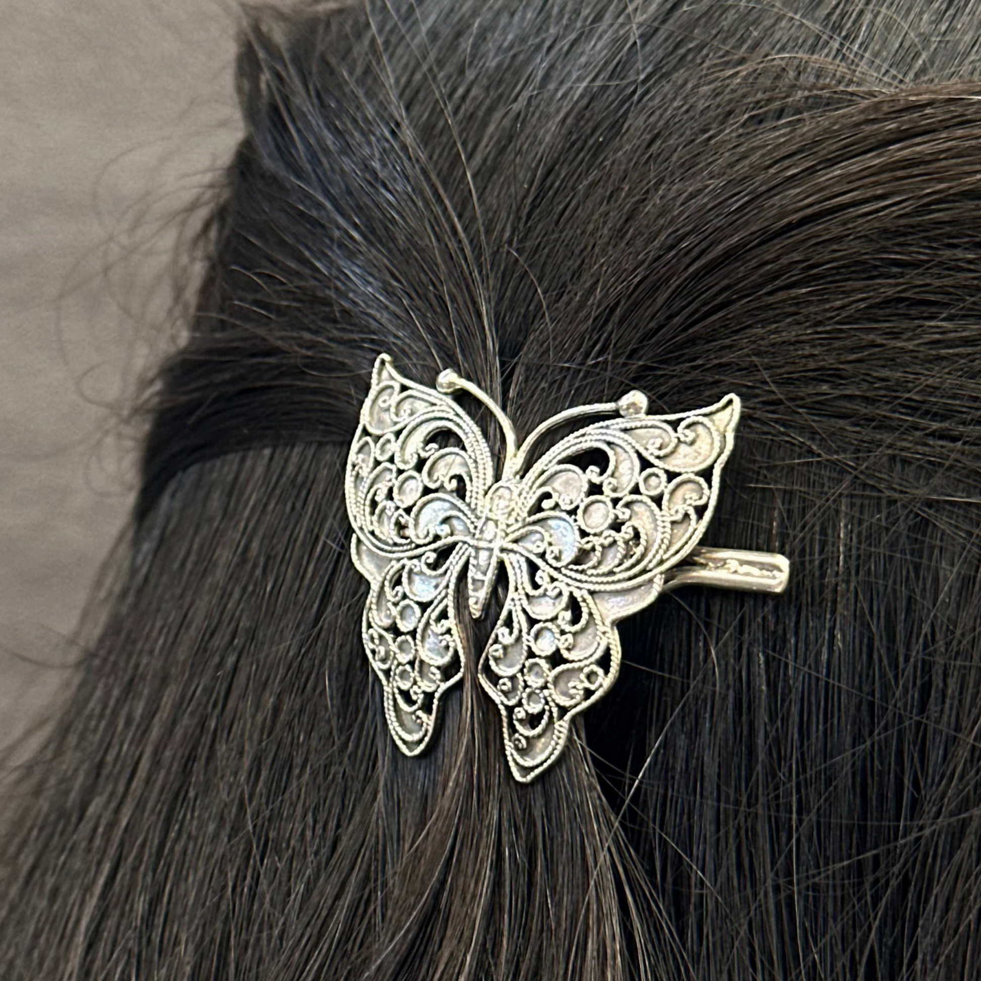 Silver butterfly hair clip on black hair against a neutral background